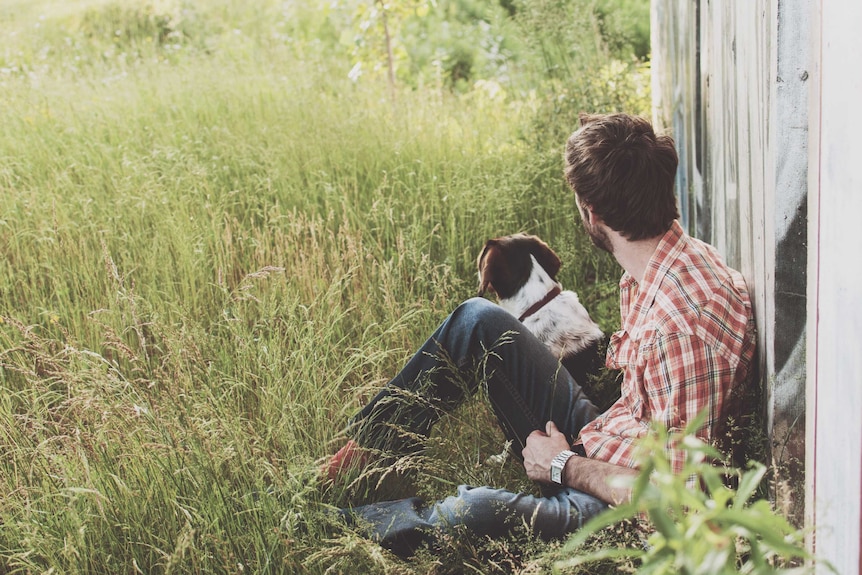 A man and his pet dog sit together staring off into the distance, offering each other support.