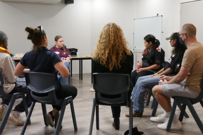 a group of young people sit on chairs in a circle in a room