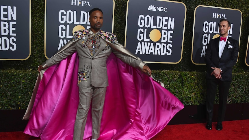 Billy Porter poses with a grey cape lined with pink silk on the red carpet.