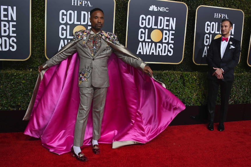 Billy Porter poses with a grey cape lined with pink silk on the red carpet.