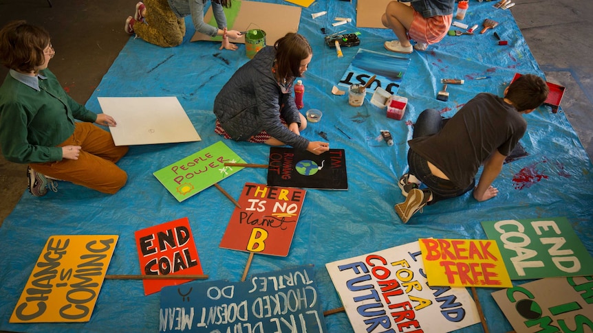 Overhead shot of students with paint and carboard, painting slogans on placards.