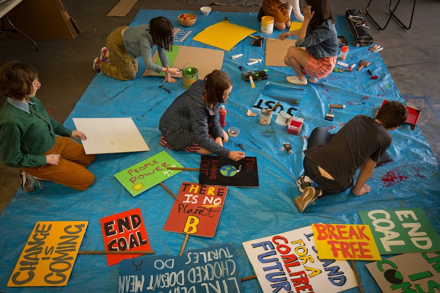 Overhead shot of students with paint and carboard, painting slogans on placards.