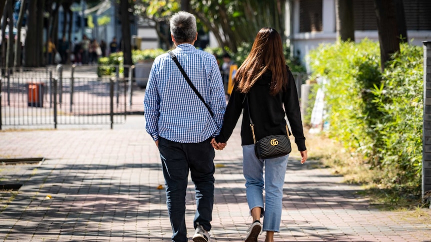 An older man walks hand in hand with a teenaged girl