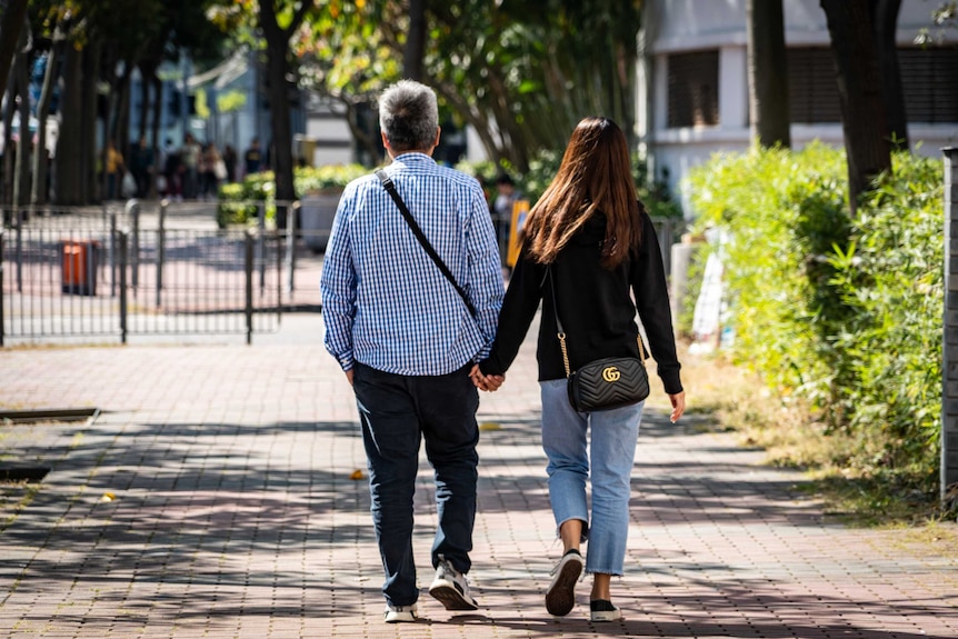 An older man walks hand in hand with a teenaged girl