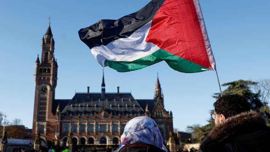 Two protesters stand outside the International Court of Justice holding the Palestinian flag