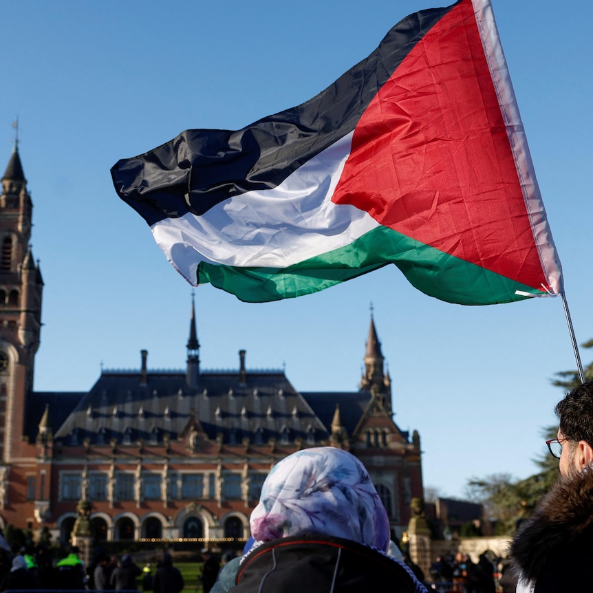 Two protesters stand outside the International Court of Justice holding the Palestinian flag