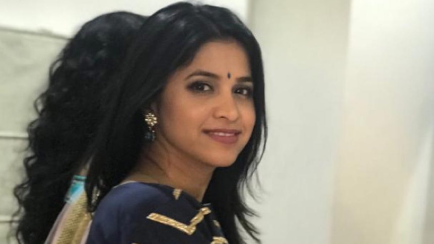 A woman stands in traditional Indian clothing and smiles at the camera.