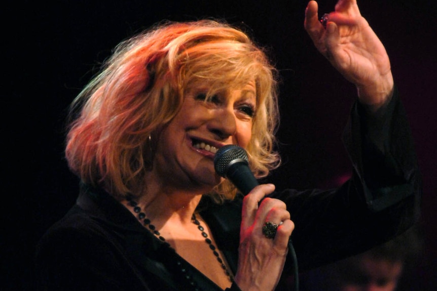 Australian singer Renee Geyer holds a microphone as she sings and raises her free hand