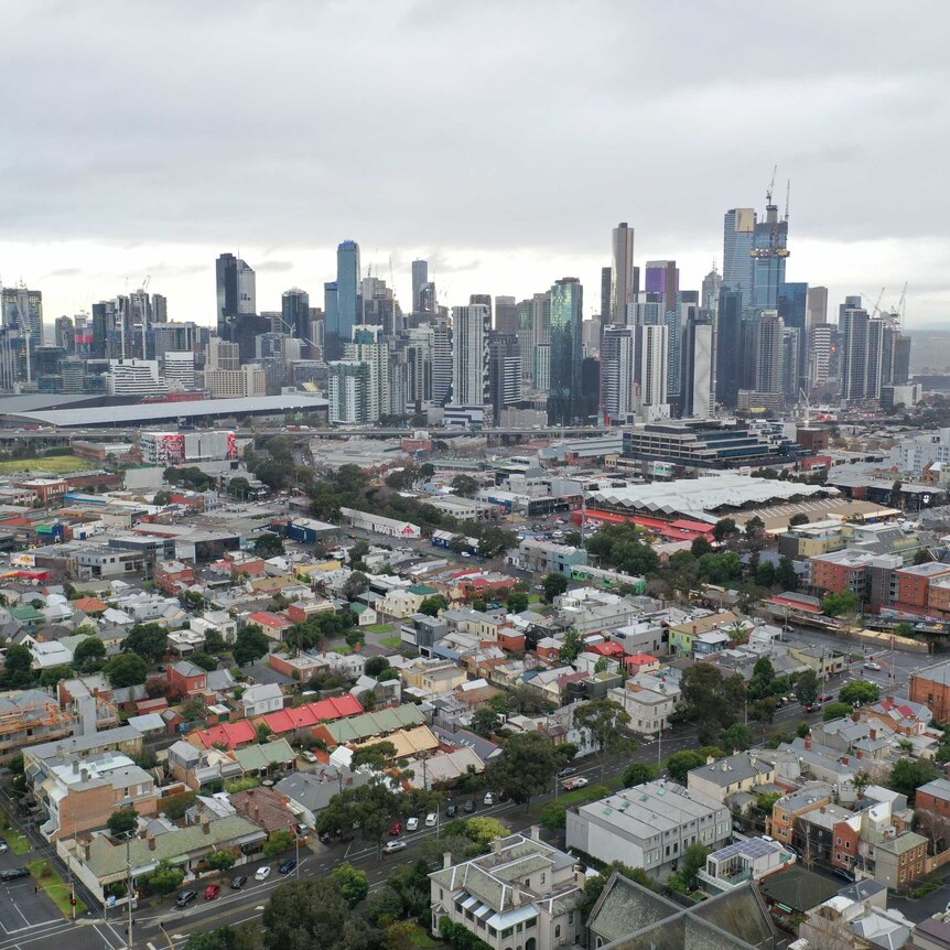 Older, low rise heritage buildings in the foreground and Melbourne's city towers in the background with a grey, cloudy sky.