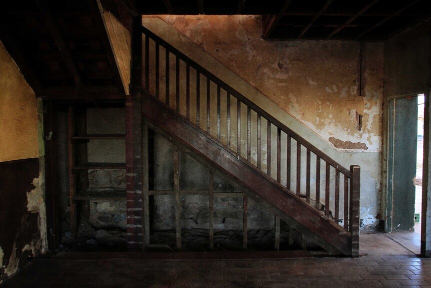 Wooden stairs in front of a wall with old, peeling paint.