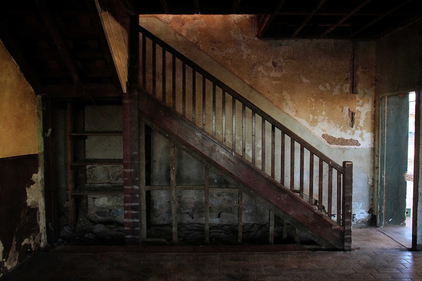 Wooden stairs in front of a wall with old, peeling paint.