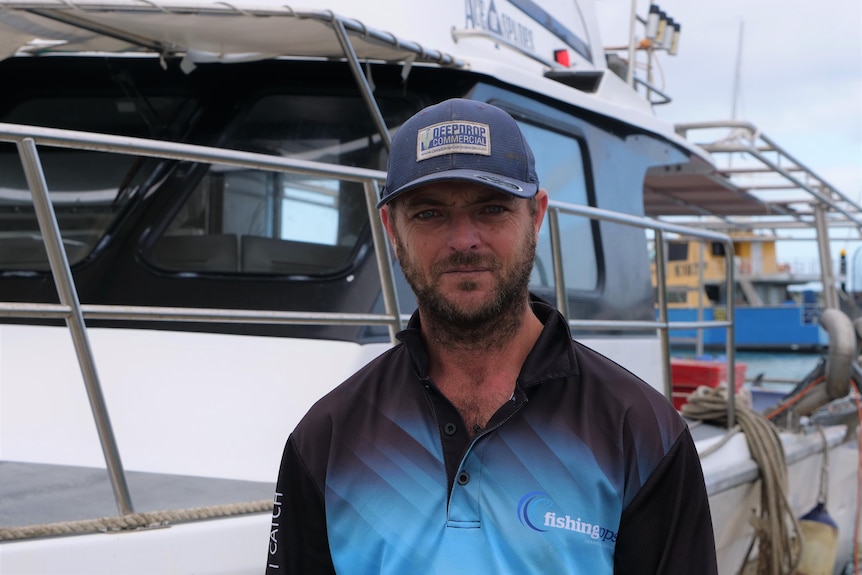 Man stands in front of his boat in the marina. 