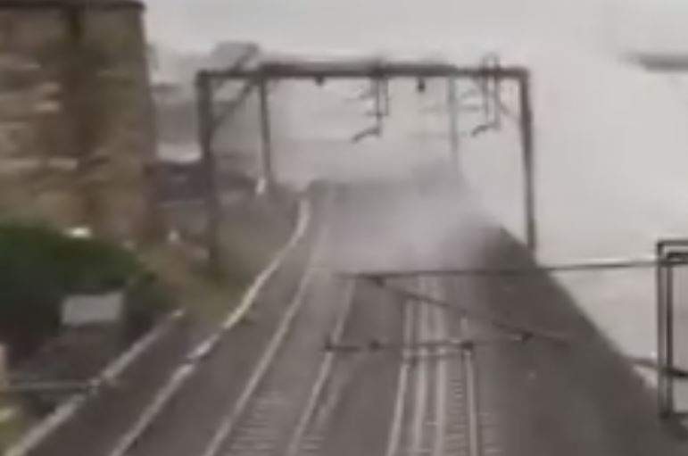 Waves crash above a seawall and over a railway line in Scotland.