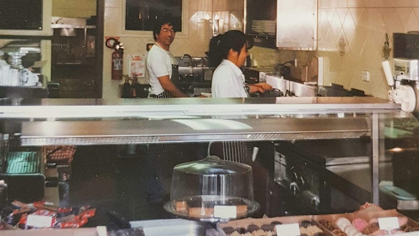 Brendan Wan's mum lifts a fryer out of the oil in and his dad looks at the camera. The couple are working in the restaurant.