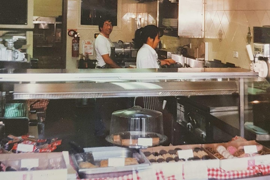 Brendan Wan's mum lifts a fryer out of the oil in and his dad looks at the camera. The couple are working in the restaurant.