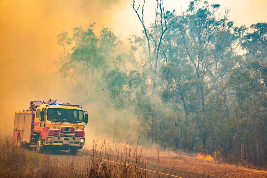 A QFES truck amidst orange smoke with a burning bush in background.
