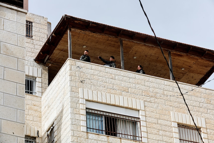 Police officers stand on the balcony of a house. 