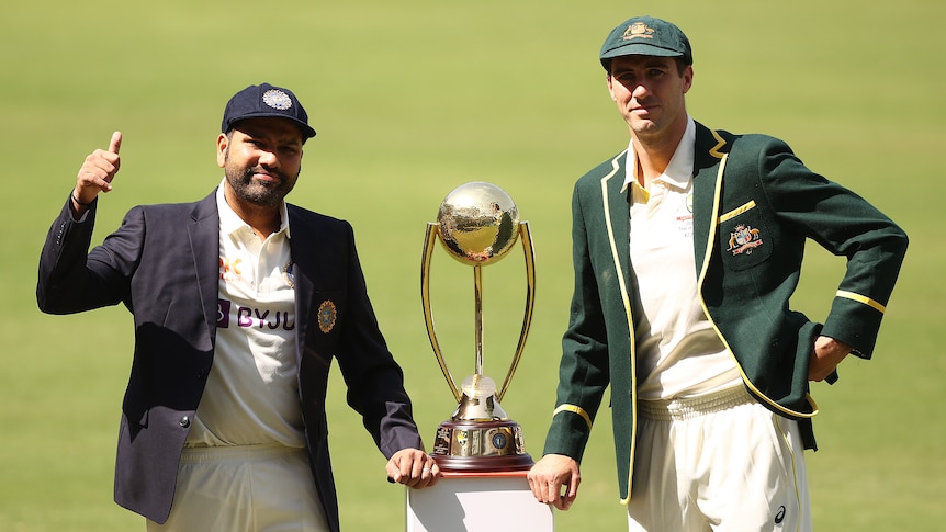 Rohit Sharma and Pat Cummins stand either side of the Border-Gavaskar trophy wearing blazers