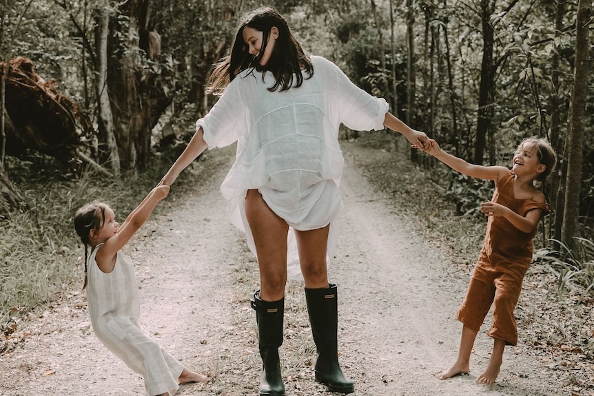 Mother Jayde Couldwell holding hands with her two children in the bush.