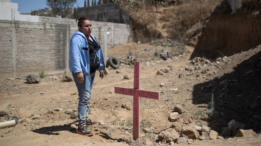 Angeles stands by a pink cross.