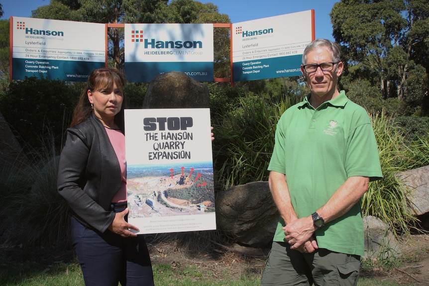 A woman holding a sign and a man in a green shirt stand in front of a sign saying Hanson
