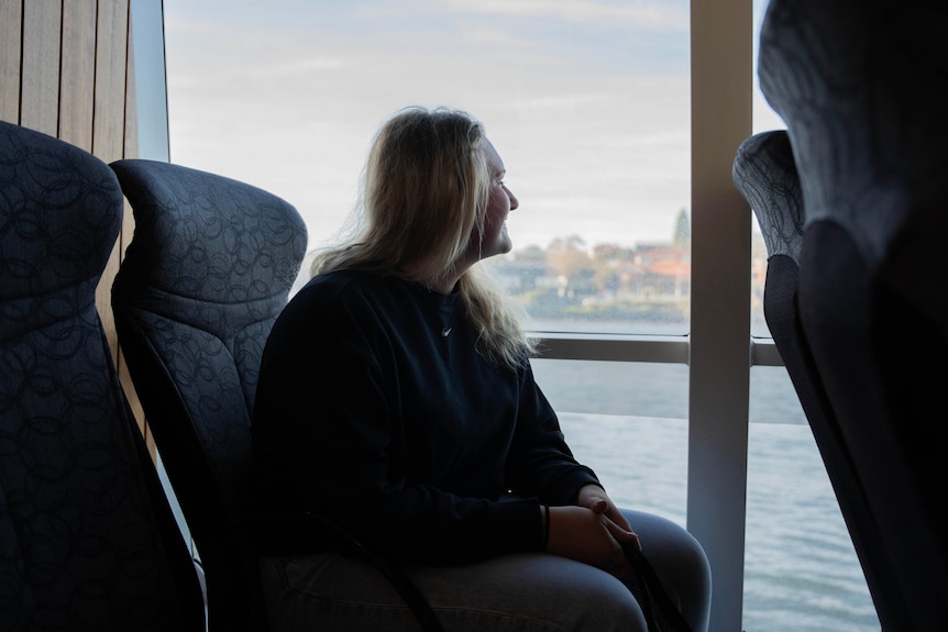 A woman with long blonde hair looks at the River Derwent through a ferry window.