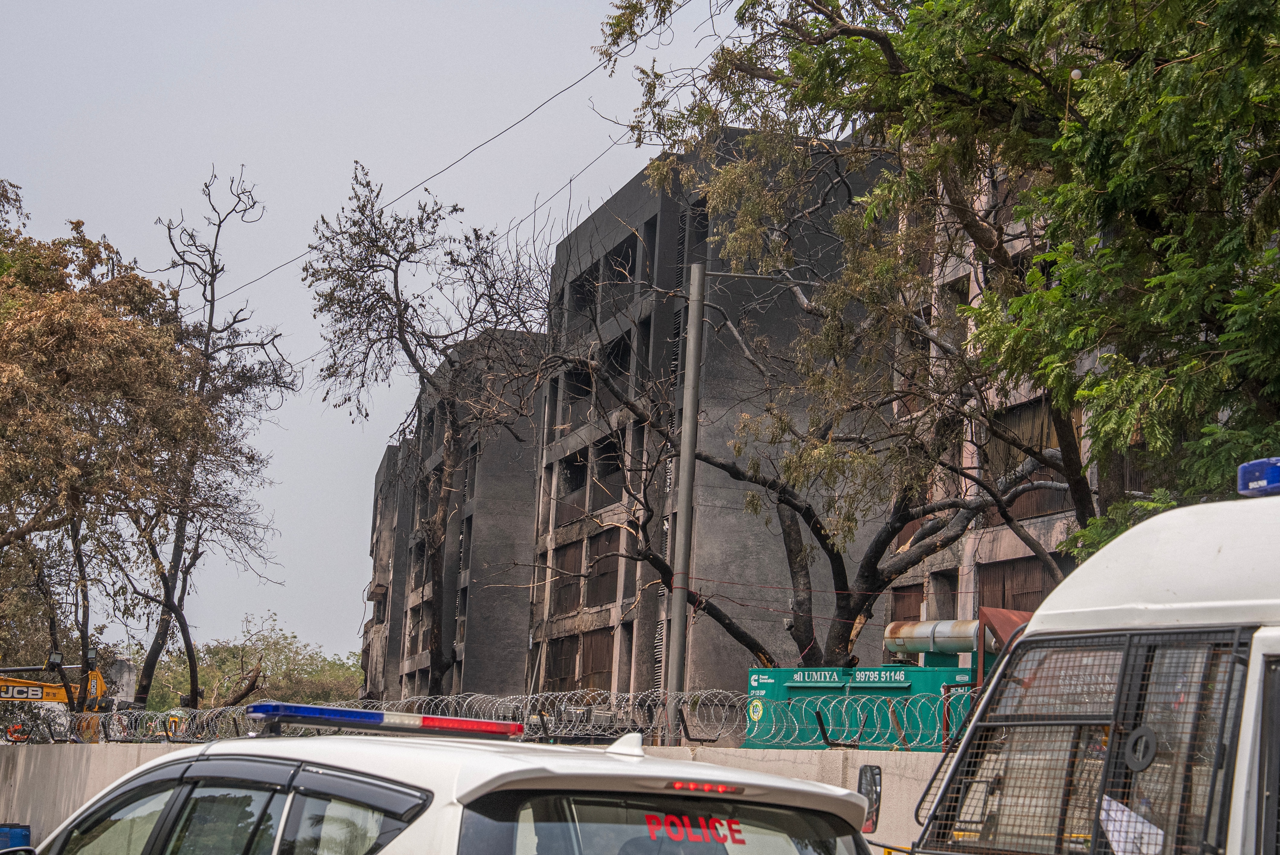 A mid-rise building partially burned out with police cars in the foreground.