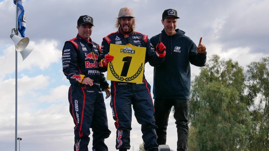 Motorsports champion Toby Price and his two teammates stand and smile after winning the 2021 Finke Desert Race.