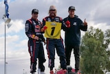 Motorsports champion Toby Price and his two teammates stand and smile after winning the 2021 Finke Desert Race.