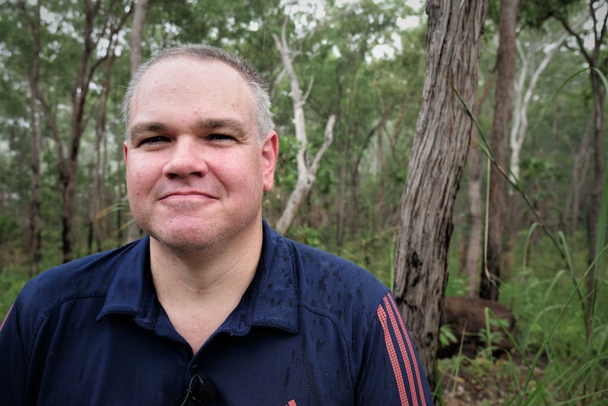 Man in bush smiling wearing navy sports shirt.