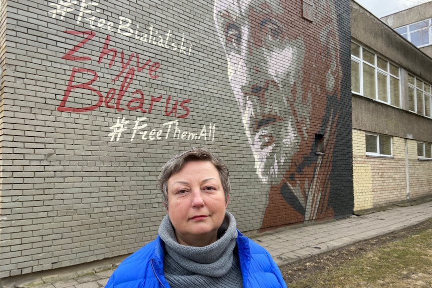 Iryna stands in front of a wall that reads 'Free Bialiatski, save Belarus, free them all' and bears an image of Bialiastkis face