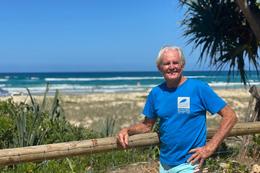 An older man leans on a fence at a Gold Coast beach