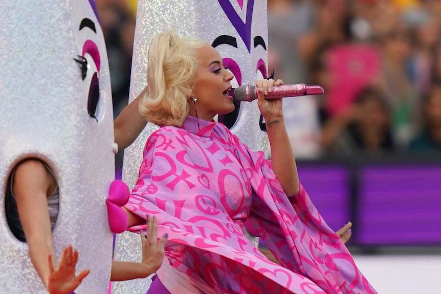 Katy Perry, surrounded by giant cricket bats with effeminate faces, sings on the MCG.