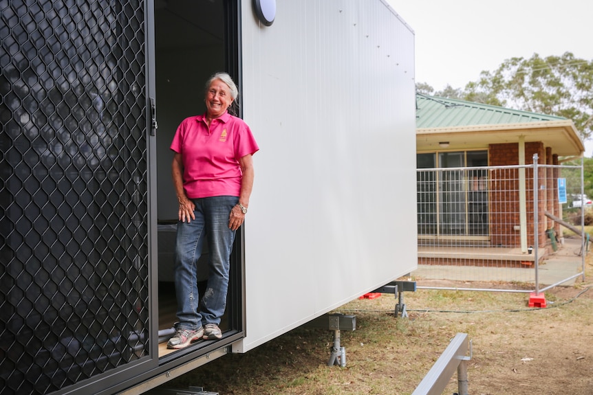 ruth nielsen in pink shirt stands in door of module home behind house