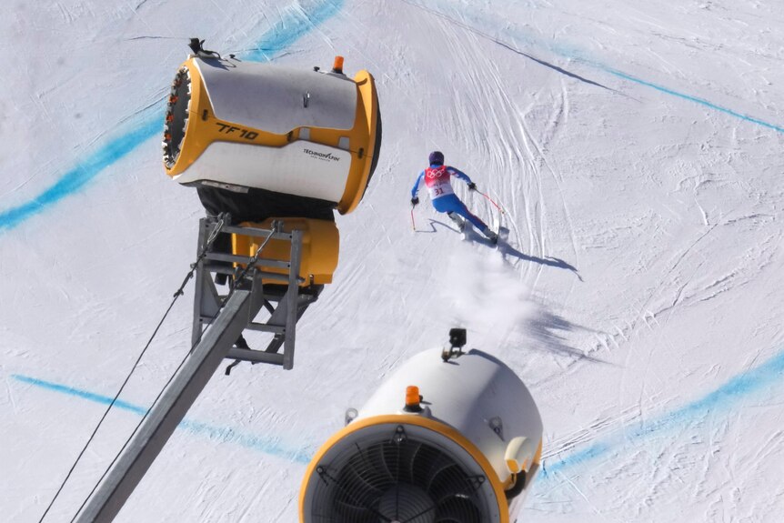 Man skis past snow making machines.