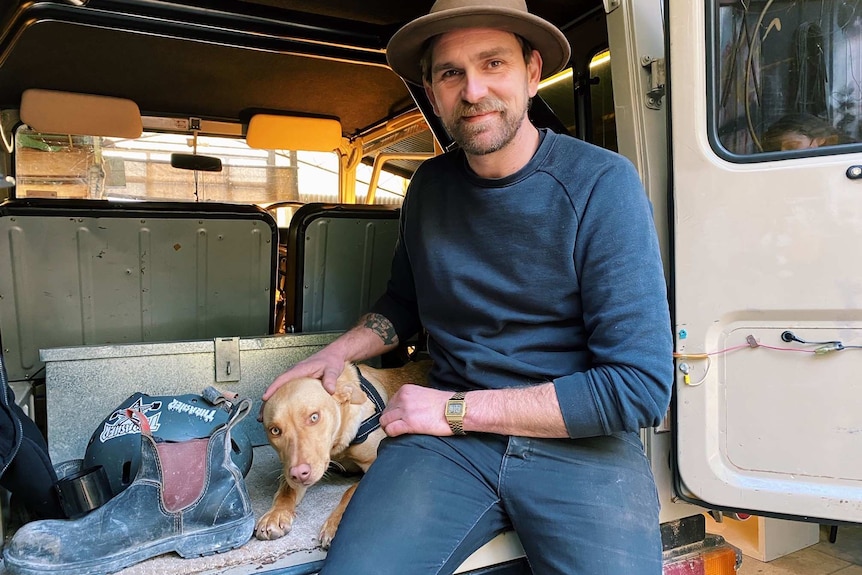 a man sits in a country van with his dog