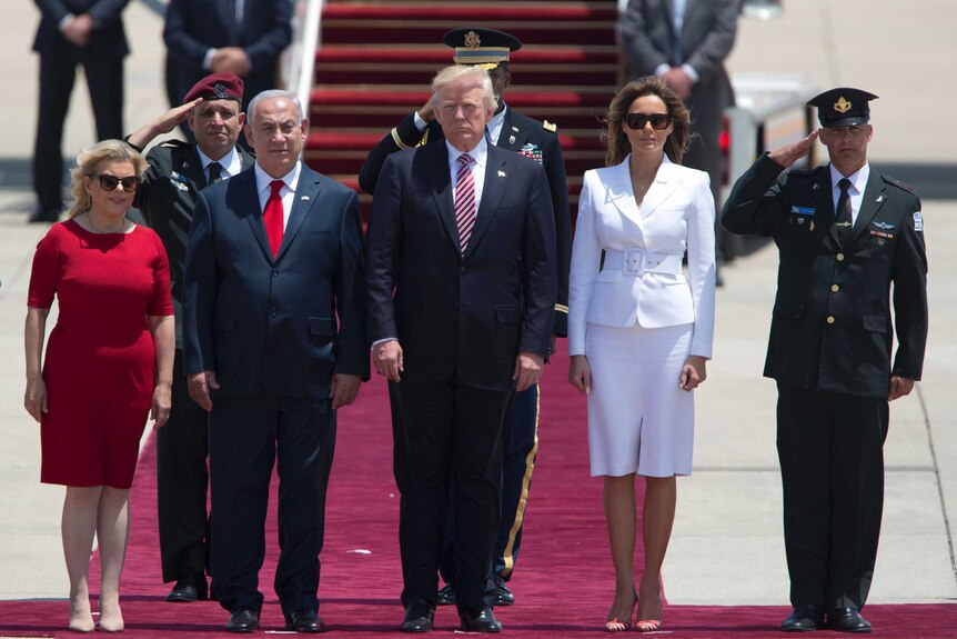 Donald and Melania Trump stand beside Benjamin and Sara Netanyahu. A red carpet, plane steps and saluting men are visible.