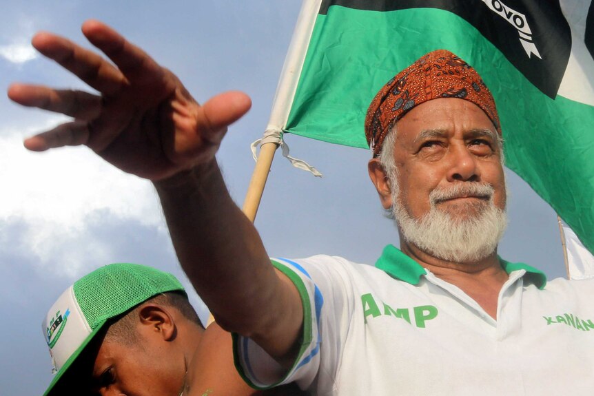 Xanana Gusmao stretches his arm out smiling while a Timorese flag flies behind him