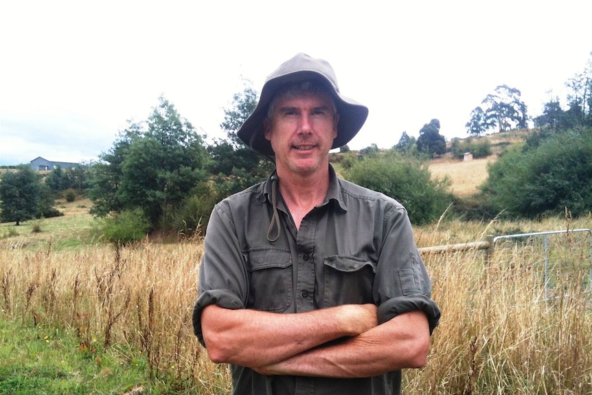 A man in khakis and sun hat with his arms crossed as he stands on a rural property.