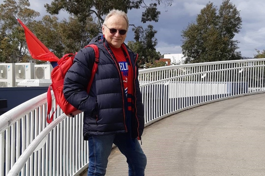 Mr Pinches wears red and blue, standing on a bridge with a red flag in his backpack.
