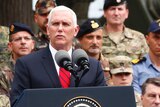 Mike Pence delivers a speech at a lectern with soldiers and others in the background.