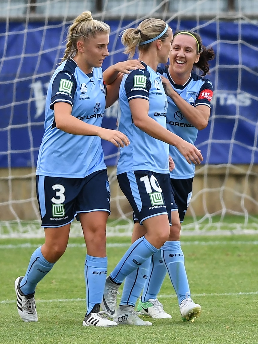 Soccer players wearing light blue jerseys celebrate after a goal is scored