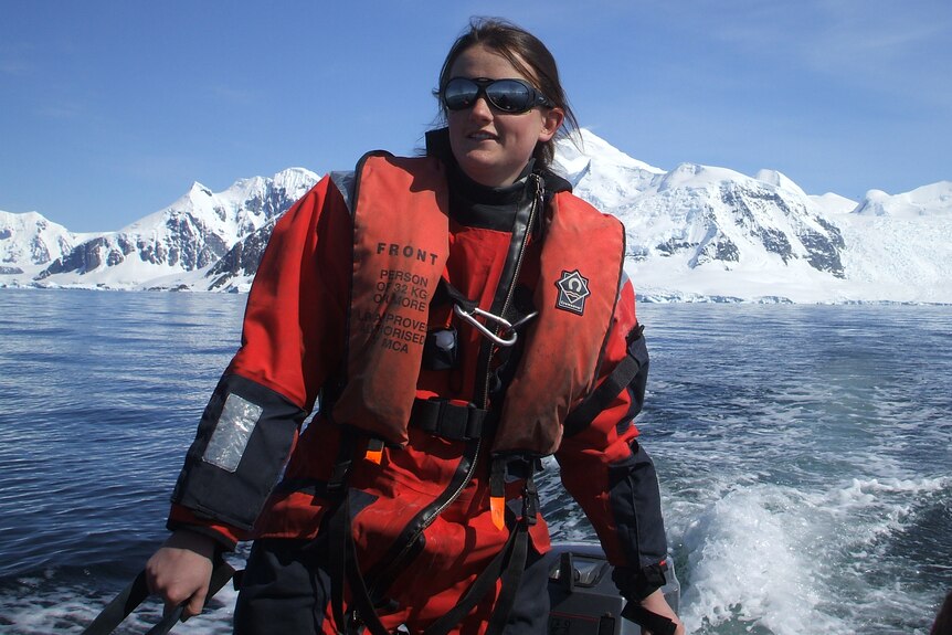 Dr Sian Henley wears a red life jacket and sits on a boat with snow-covered hills in the background