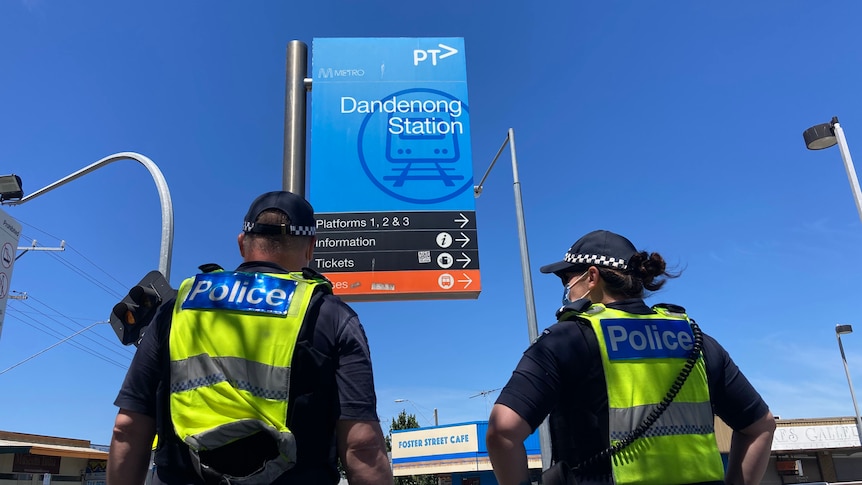 Two police officers in high-visibility jackets stand outside Dandenong train station under a blue sky.