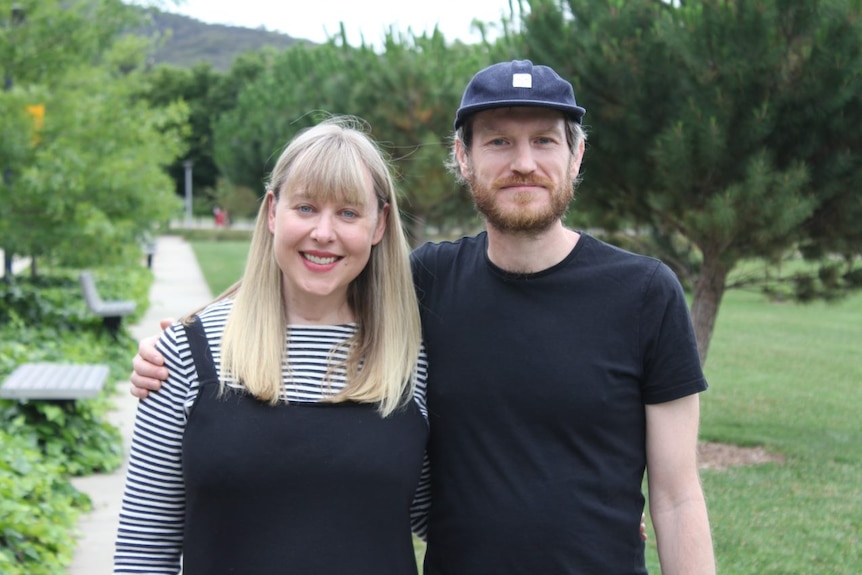 A man and a woman smile at the camera with their arms around each other.