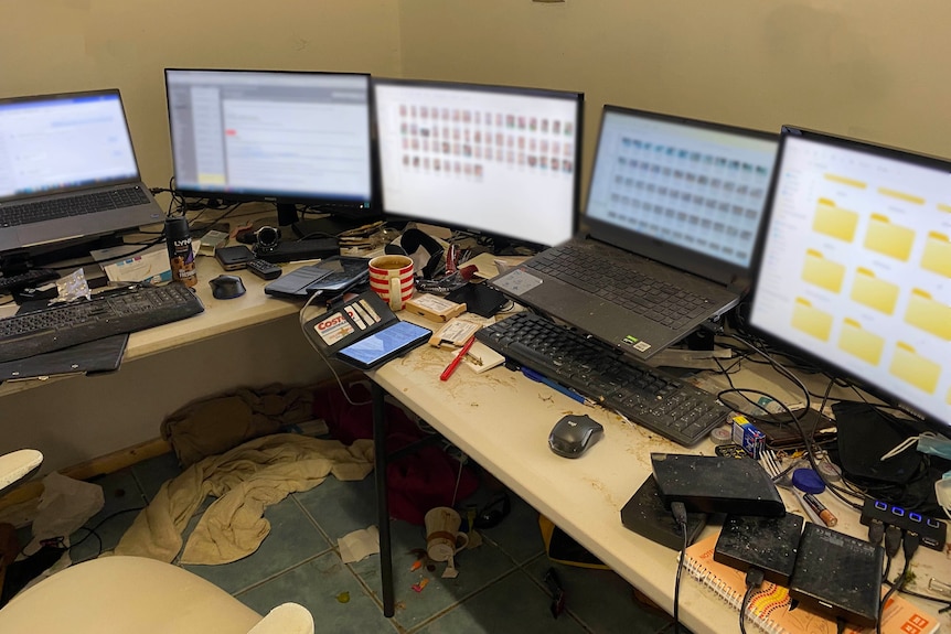 A messy desk with five computer monitors and laptops on it.