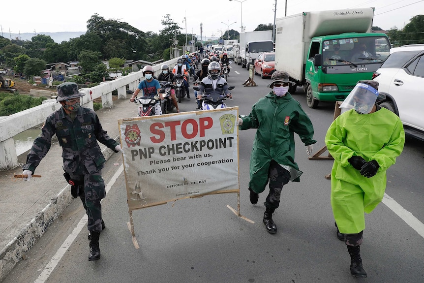 Two men in fatigues carry a sign saying 'Stop: PNP checkpoint' ahead of a long line of traffic.