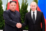 Two men in suits shake hands as the stand in front of North Korean and Russian flags