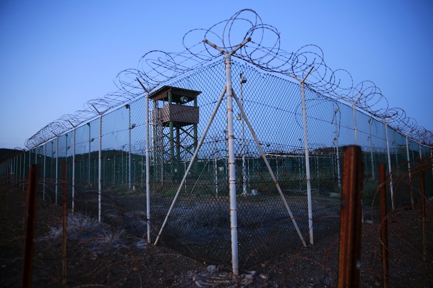 A barbed wire fence and a watch tower before a blue sky at dusk 