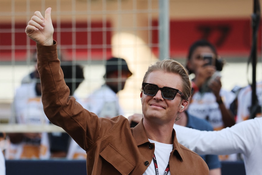 A man wearing sunglasses gives a thumbs-up to a crowd. 